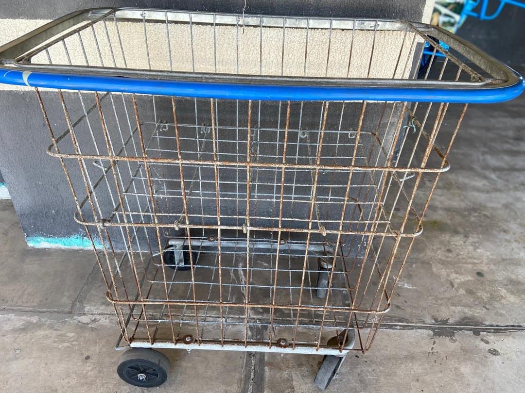 Carrinho de zelador enferrujado, com pintura descascada e rodízios gastos antes da reforma.